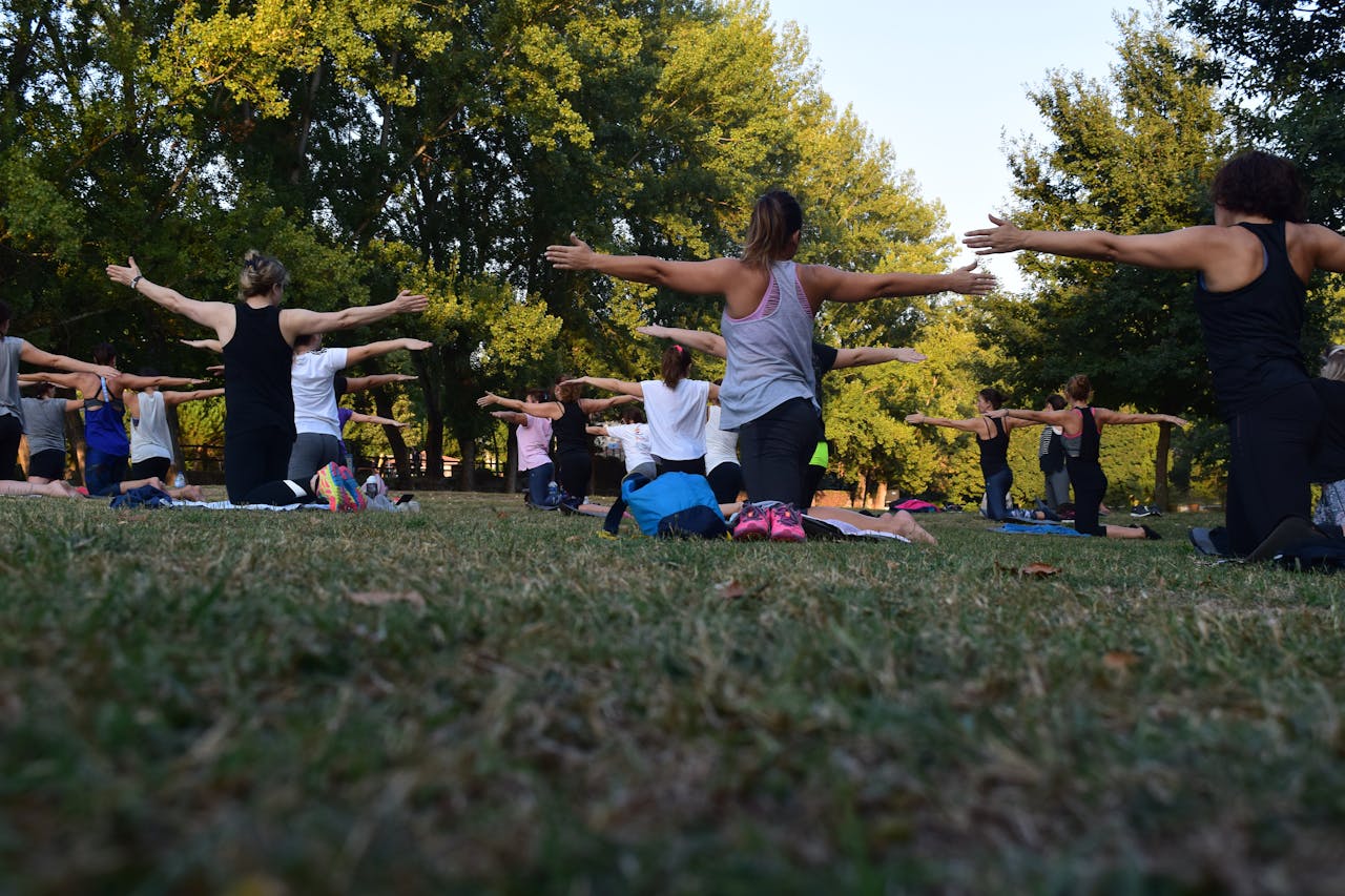 hero-img-01 Group of adults practicing yoga outdoors in a park surrounded by trees.