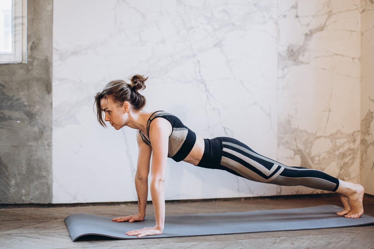 gallery-3 A woman performing a plank pose on a yoga mat indoors, showcasing strength and focus.