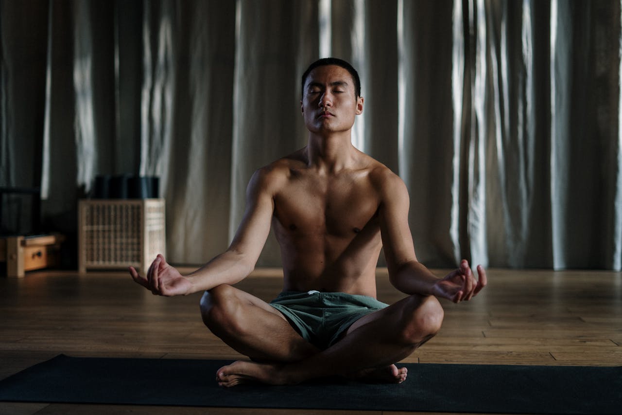 gallery-6 Shirtless asian man practicing yoga in meditation pose at home for wellness.